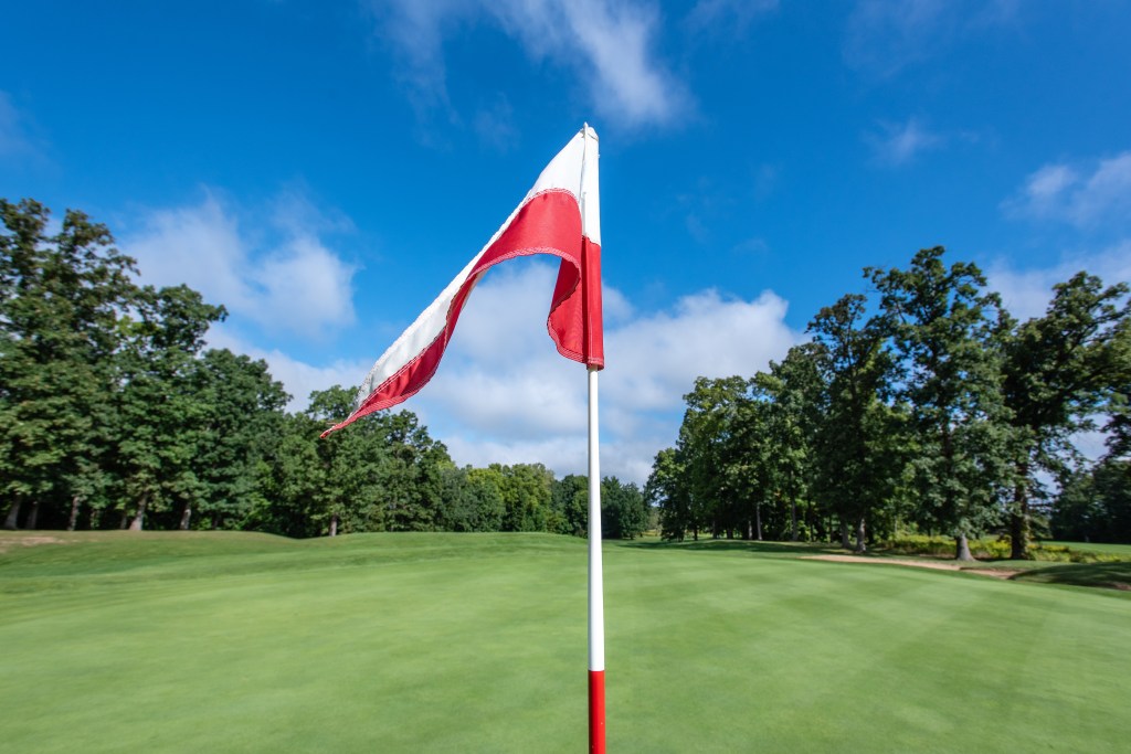 White and red flag front and center at the course, trees in the background.